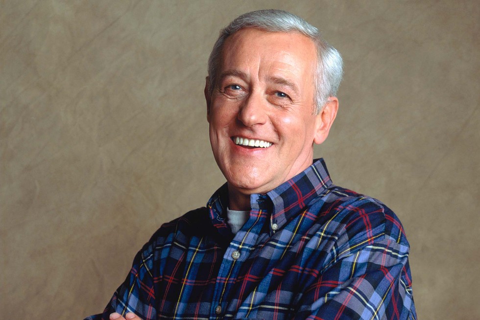 john-mahoney-frasier John Mahoney stands with his arms crossed, smiling for the camera
