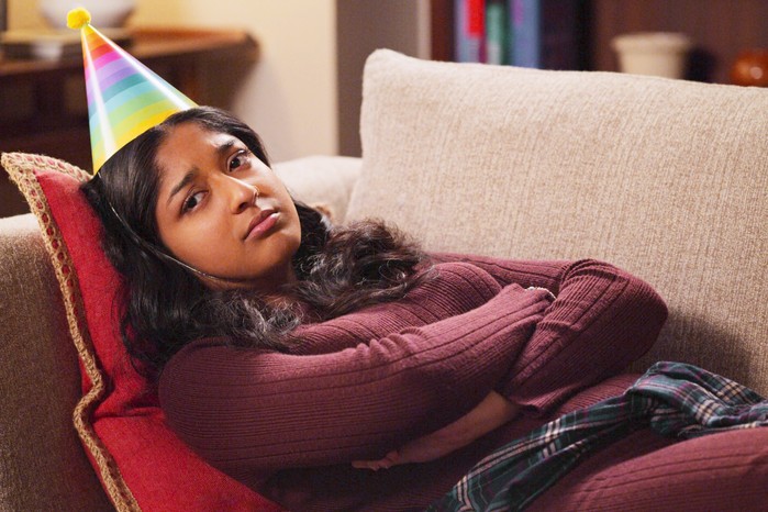 never have i ever A sad Devi lying on a sofa wearing a party hat